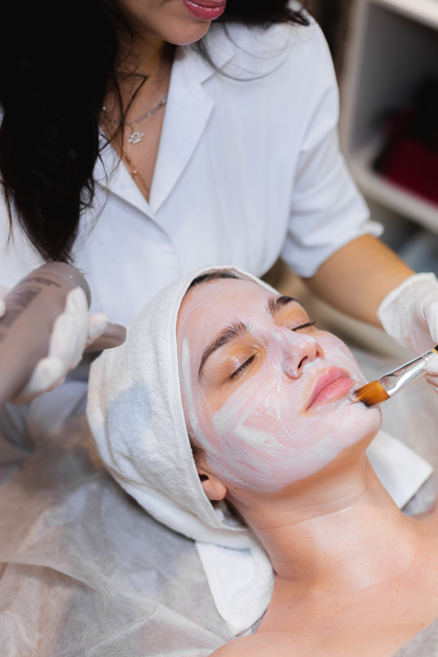 beautician with brush applies white moisturizing mask face young girl client spa beauty salon scaled